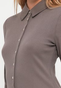 Figurvänlig ribbad topp i taupe med krage och knappslå fram med små, ljusa knappar.