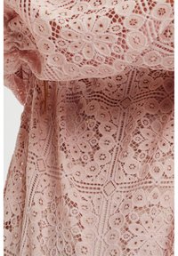 Rosa spets tyg med intrikata blommönster och en strukturerad yta. Designen inkluderar geometriska former och öppna vävningar.