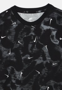 Juoda marškinėliai su reljefiniu raštu ir išmėtytais baltais „Nike“ logotipais. Apvali iškirptė ir trumpomis rankovėmis. Minkšta medvilnė.