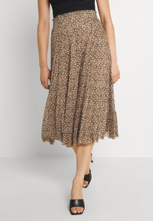 Vrouw draagt een bruine bloemenprint midi rok gecombineerd met zwarte open-teen hakken en een zwart mouwloos topje, staand tegen een effen witte achtergrond.