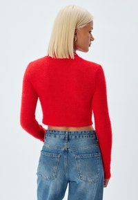 Maglione rosso corto con una texture soffice e maniche lunghe, abbinato a jeans di denim azzurro chiaro a vita alta con tasche posteriori.