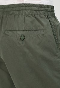Pantaloni corti verdi in tessuto con vita elasticizzata, tasca sul retro con chiusura a bottone e finitura liscia.