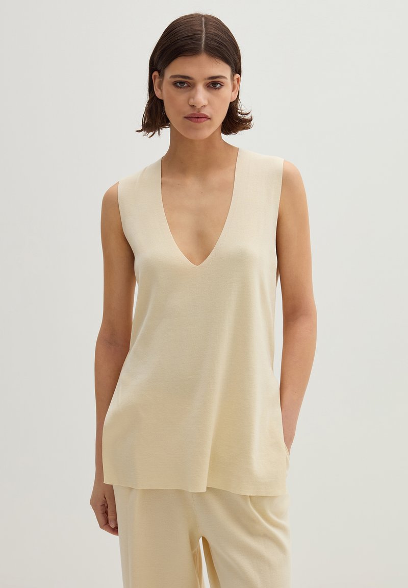 Beige ärmelloses Top mit tiefem V-Ausschnitt, aus glattem Stoff, mit lockerer Passform und subtiler Textur, kombiniert mit passenden beigen Hosen.