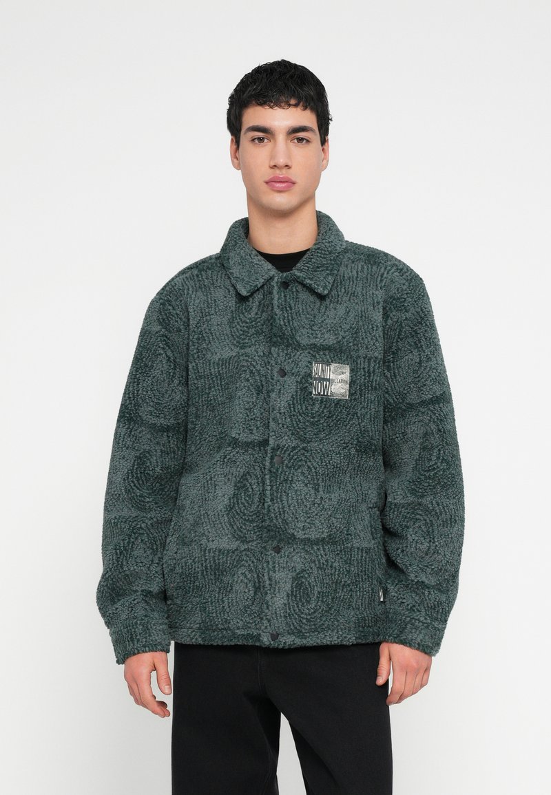 Πράσινο, υφασμάτινο μπουφάν fleece με γιακά, κουμπωτό κλείσιμο και μια τσέπη με κέντημα που διαθέτει γραφικό σχέδιο στο αριστερό στήθος.