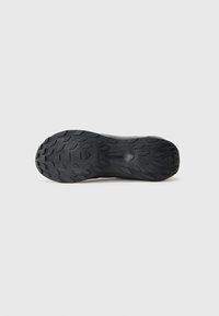 Black athletic shoe outsole featuring a textured rubber surface with a zigzag pattern and prominent lugs for traction.