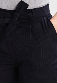 Marinrandiga byxor i en texturerad tyg, med ett knytbart midjebälte och två framfickor med subtila veck.