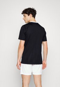 Svart sportskjorta med kort ärm och vit krage, tillverkad av en slät tyg, visad från baksidan, kombinerad med vita shorts.