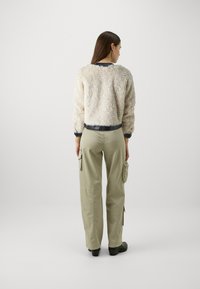 Maglione di cotone con texture cremosa e orlo nero a costine, abbinato a pantaloni cargo verde oliva con tasche laterali e orli alla caviglia. Scarpe nere.
