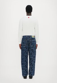 White long-sleeve shirt with a red accent on the back, paired with blue denim pants featuring a repeating "ICECREAM" pattern. Black footwear.