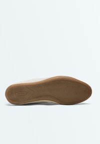 Semelle de chaussure avec une accroche en caoutchouc brun texturé, logo ovale "OYSHO" près du talon, et lignes de contour lisses sur un fond neutre.