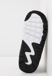 Sola de sapatilha Nike com um design em borracha preta, apresentando um padrão central ondulado em branco e uma textura para aderência, rotulada como "NÃO MARCANTE".