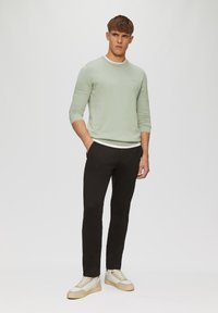 Pull en tricot vert menthe avec un col rond, associé à un pantalon slim noir et des baskets avec des accents beiges.