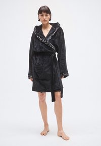 Albornoz negro de felpa con capucha, con un ribete decorativo brillante a lo largo del cuello. Incluye cinturón de cintura y bolsillo frontal.