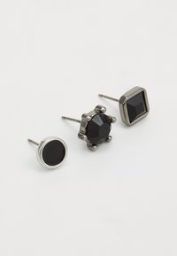 Three black stud earrings: one round, one cushion-cut with a prong setting, and one square, all set in metallic hardware.