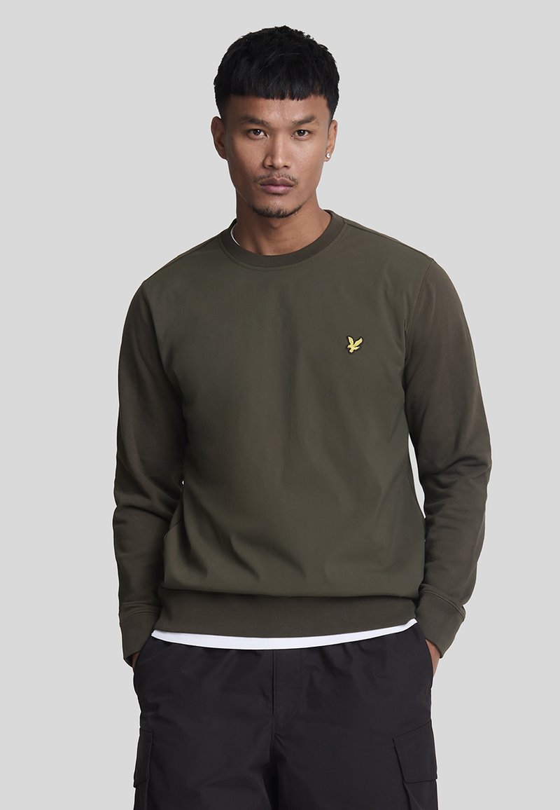 Sweatshirt verde oliva con collo a girocotolo a coste, maniche lunghe e un piccolo logo di un'aquila gialla sul petto. Tessuto di una consistenza liscia.