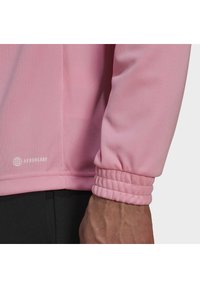 Rosa idrottslångärmad tröja med texturerad tyg och elastiska manschetter. AEROREADY-logotypen visas nära fållen.