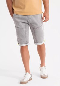 Pantalones cortos de mezclilla gris con dobladillos enrollados, que presentan bolsillos delanteros y traseros y un sutil acento verde en los dobladillos. Combinados con zapatillas blancas.
