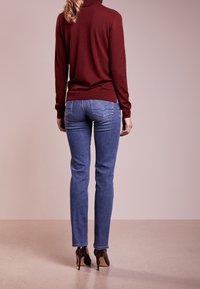 Marin turtleneck tröja och ljusblå jeans, figursydd form, slät textur. Bruna högklackade skor, raka jeans med subtila sömdetaljer.