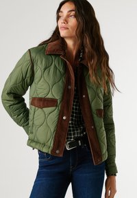 Quilted green jacket with brown corduroy collar and pockets, featuring metallic buttons, worn over a plaid shirt and blue jeans.