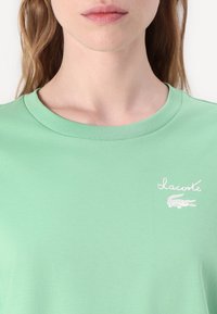 Grønn bomull t-skjorte med rund hals, med en hvit Lacoste-logo og krokodille-design. Glatt tekstur, uformell passform.