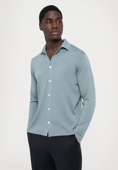 Camisa de botão de manga longa azul clara com colarinho e pala frontal, apresentando botões brancos e um padrão de malha texturizada.