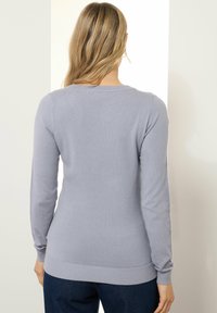 Lichtgrijze lange mouwen sweater, zachte textuur, getailleerd ontwerp, geribbelde manchetten en zoom, schoon silhouet met een subtiele halslijn.