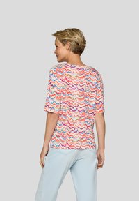 Short-sleeve shirt featuring a multicolored zigzag pattern on a light background. Soft texture with a relaxed fit, paired with light blue pants.
