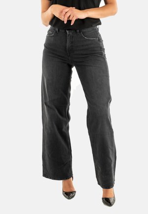 Jean large noir en denim, avec un design classique à cinq poches, présentant des décolorations légères et des détails de couture. Associé à des chaussures noires.