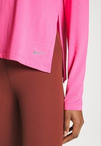 Rosa långärmad topp med sidofickor och en liten grå Nike-logga. Matchad med bruna leggings som har ett mjukt och elastiskt material.