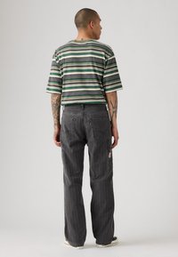 Camisa de manga corta a rayas en verde y gris; pantalones de mezclilla gris con bolsillos de parche; ajuste casual con detalles de costura visibles.