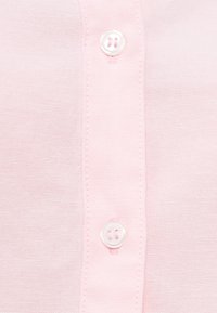 Ύφασμα ανοιχτό ροζ πουκάμισου με λεία υφή, δύο λευκά κουμπιά και εμφανείς ραφές κατά μήκος της λωρίδας κουμπώματος.