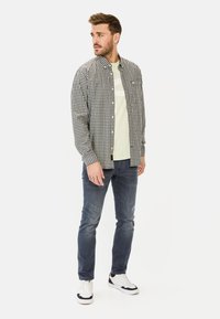 Zwart-wit geblokte shirt met een button-down kraag over een lichtgroen t-shirt, gecombineerd met blauwe jeans en witte sneakers.