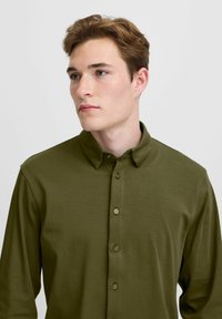 Olive green button-up shirt with long sleeves, soft texture, point collar, and five buttons down the front. Simple, clean design.