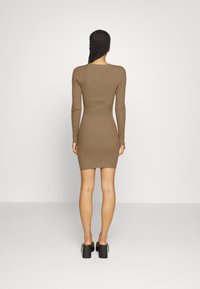 Abito lungo a maniche lunghe di colore marrone a coste, con un design aderente che arriva fino a metà coscia, abbinato a tacchi alti neri a pianta chunky.