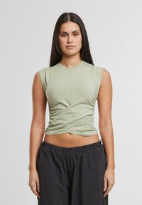 Olijfgroene mouwloze top met een aansluitend ontwerp en geplooide zijkant, gecombineerd met losse zwarte broek met een elastische tailleband.