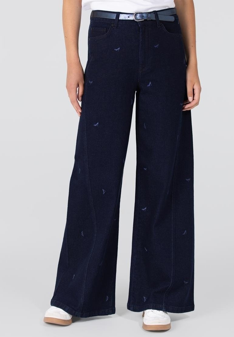 Wijduitlopende donkerblauwe jeans van denim met subtiele vogelpatronen. Vergezeld door een blauwe riem en witte sneakers.