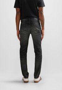 Jeans de mezclilla negra con un corte ajustado, que cuentan con bolsillos traseros, un ligero desgastado y una cinturilla con marca, combinados con zapatos claros.