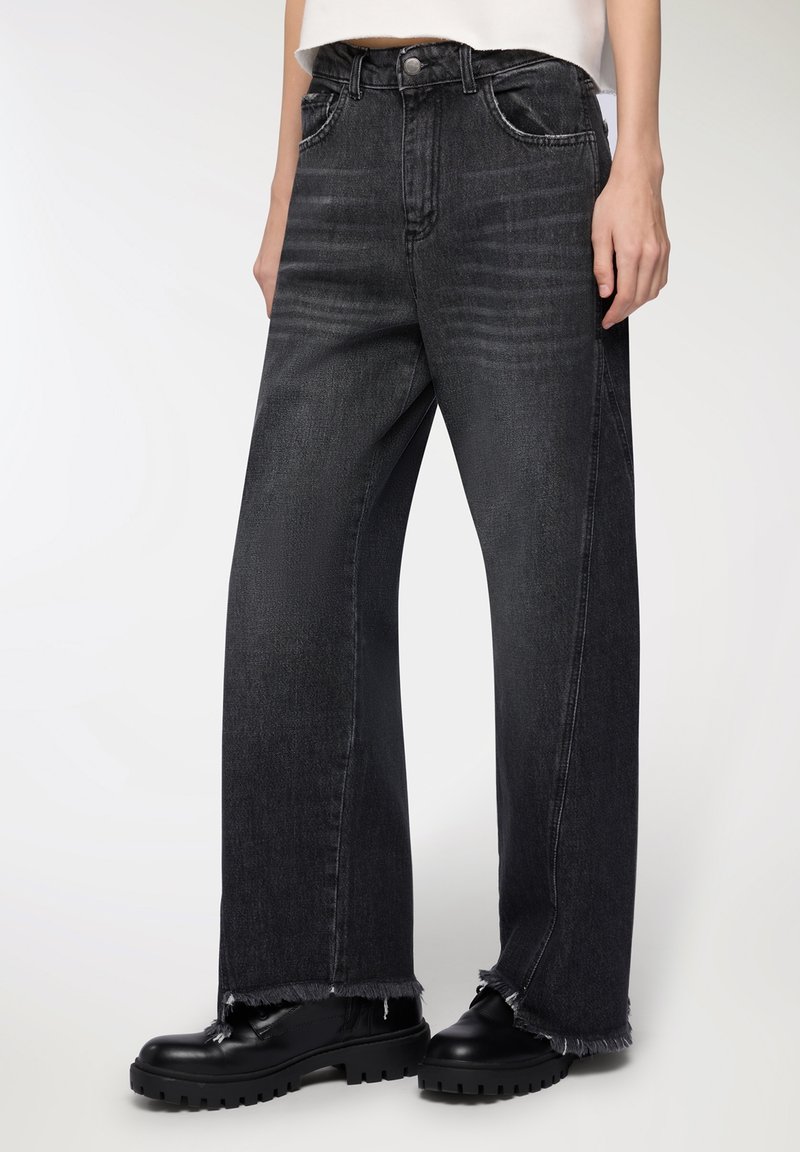 Jeans neri a gamba larga con orlo sfrangiato, caratterizzati da un design classico con cinque tasche e una leggera scoloritura. Abbinati a calzature nere robuste.