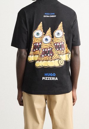 Dos d'un t-shirt noir avec trois tranches de pizza cartoon, chacune avec un gros œil et des dents acérées, texte « Pizza Love Extra Cheesy » et « Hugo Pizzeria ».