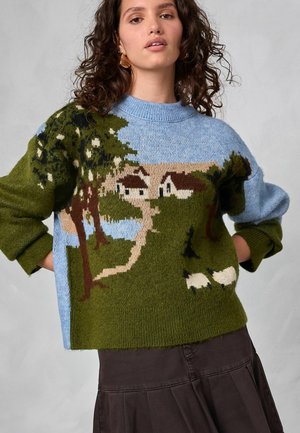 Maglione in lana con motivo paesaggistico che presenta alberi, case e pecore. Sfondo a gradiente di colore che va dal blu al verde, con scollatura rotonda e vestibilità ampia.