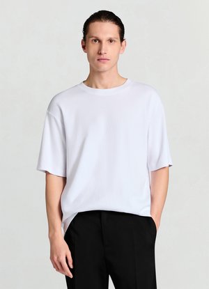 Weißes T-Shirt mit kurzen Ärmeln und Rundhalsausschnitt, mit weicher Textur und lockerem Schnitt, kombiniert mit schwarzen Hosen.