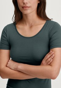 Top a maniche corte in verde scuro, realizzato in morbido tessuto elasticizzato con scollatura rotonda e superficie liscia, caratterizzato da una silhouette aderente.