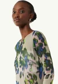 Langärmlige Bluse aus leichtem Stoff mit einem mehrfarbigen Blumenmuster auf einem hellbeigen Hintergrund und einem runden Halsausschnitt.