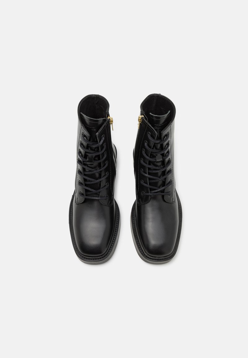 Bottines noires en cuir avec lacets, finition lisse, bout carré et fermetures éclair dorées. Côtés texturés et coutures renforcées.