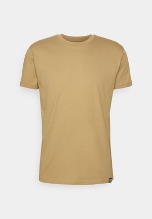 Beige short-sleeve crew neck T-shirt with a small striped tag at the bottom hem on a plain light gray background.