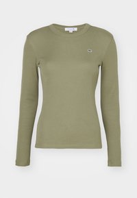 Langärmliges, olivgrünes, geripptes T-Shirt mit Rundhalsausschnitt und kleinem gesticktem Logo auf der linken Brust. Weicher Stoff, figurbetonte Passform.