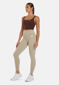 Smeđi skraćeni top i svijetlosmeđi legging visokog struka. Legging imaju logotip na kuku. Model nosi bijele sportske tenisice.