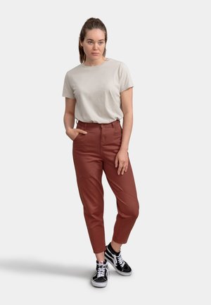 Beige short-sleeve t-shirt paired with rust-colored trousers. Trousers feature side pockets and a seam detail. Black and white sneakers complete the look.