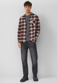 Czerwona i biała koszula flanelowa w kratę, nałożona na szary T-shirt, w połączeniu z ciemnymi dżinsami i czarnym obuwiem. Posiada kieszeń na piersi.