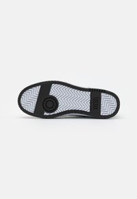 Semelle de sneaker en caoutchouc noir avec un motif en zigzag, présentant un design circulaire central et un bord texturé. Nom de la marque "DIESEL" embossé sur le côté.